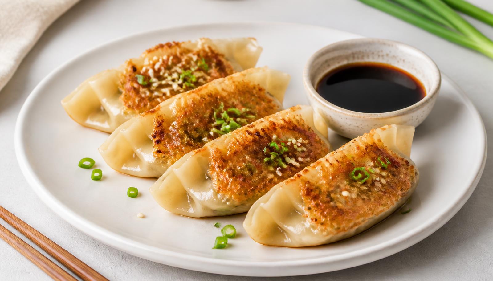 Pan-fried dumplings garnished with scallions beside a cup of soy dipping sauce