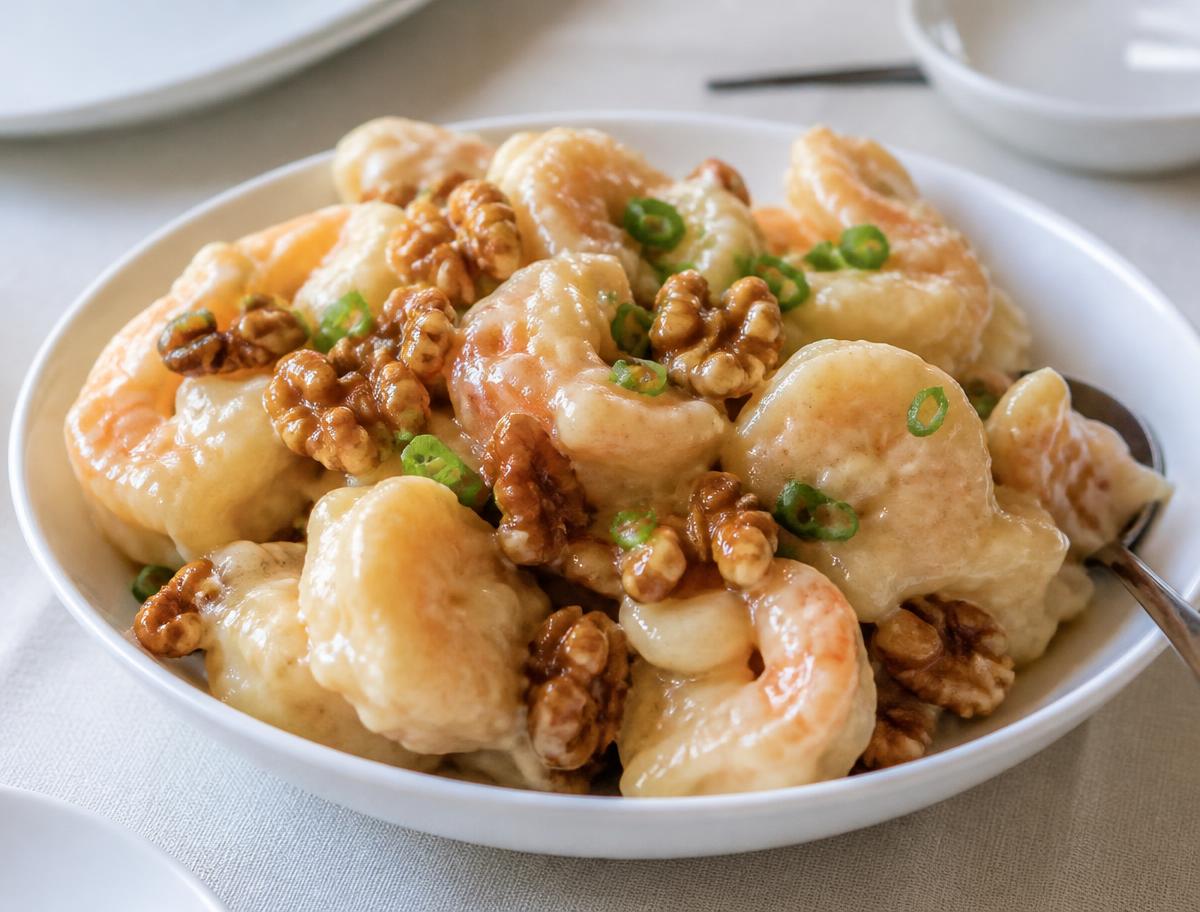 Honey walnut shrimp in a creamy honey glaze with candied walnuts and scallions in a white bowl